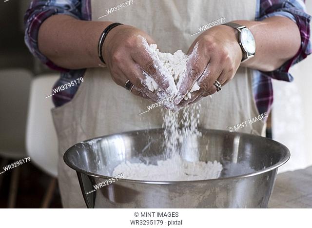 Close up of person wearing apron standing in kitchen, mixing ingredients for a crumble in metal bowl