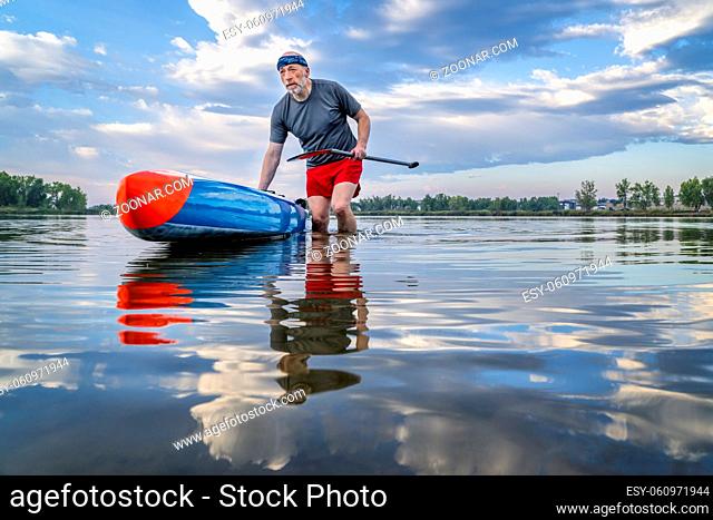 senior male stand up paddler is launching his paddleboard on a lake for morning workout in northern Colorado, solo paddling as a form of social distancing