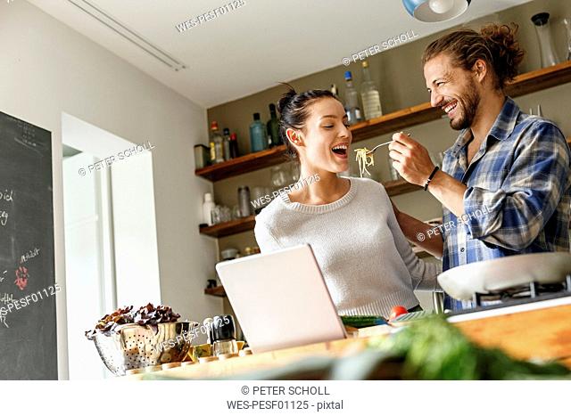 Young couple preparing spaghetti together, using online recipe