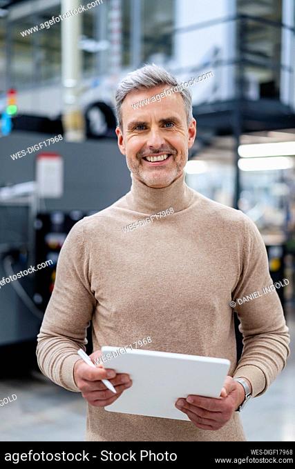 Portrait of smiling businessman holding digital tablet in factory