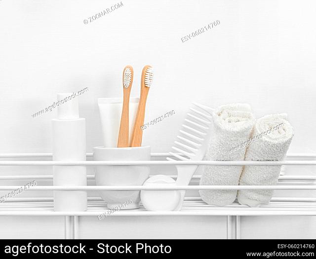 Close up beauty care and personal hygiene products and towels, toothbrushes and comb, on bath shelf over white bath background, low angle view