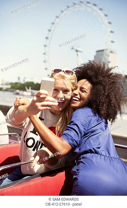 Enthusiastic friends taking selfie on double-decker bus with London Eye in background
