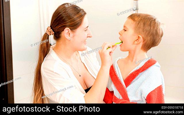 Portrait of smiling mother brushing teeth of her little son in bathroom. Concept of child hygiene and healthcare at home