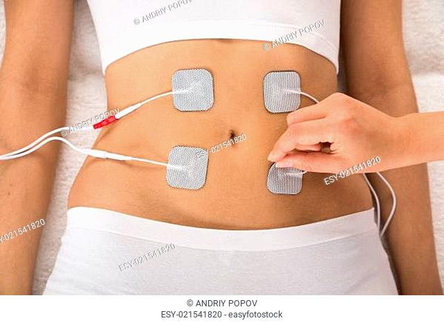 High Angle View Of Therapist Placing Electrodes On Woman's Stomach