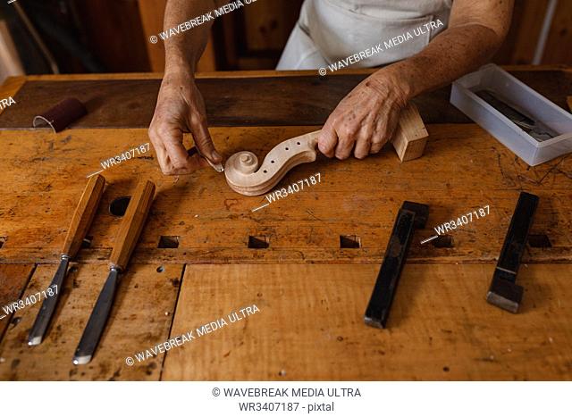 Front view mid section of a senior Caucasian female luthier working on the scroll of a violin on a workbench in her workshop, with tools in the foreground