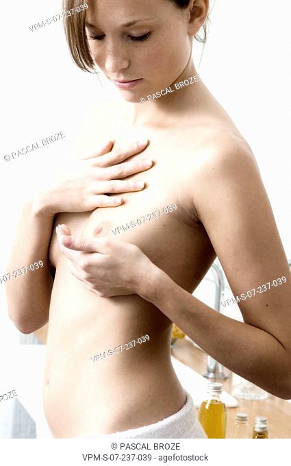 Close-up of a naked young woman massaging her breast with massage oil