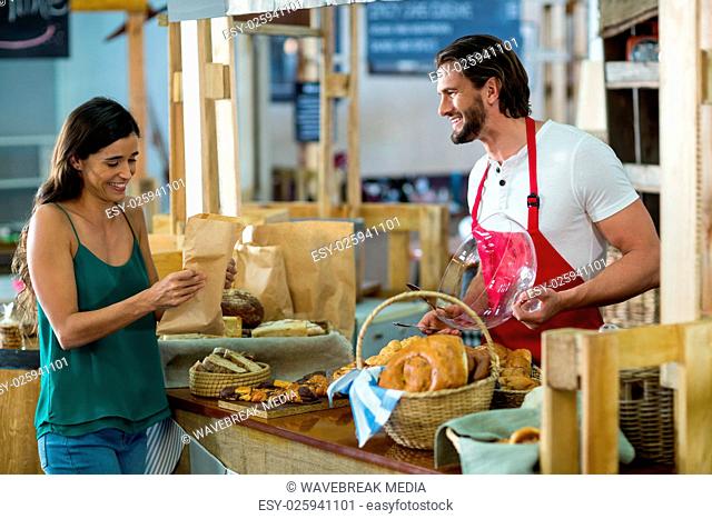 Smiling female customer receiving a parcel from bakery staff at counter