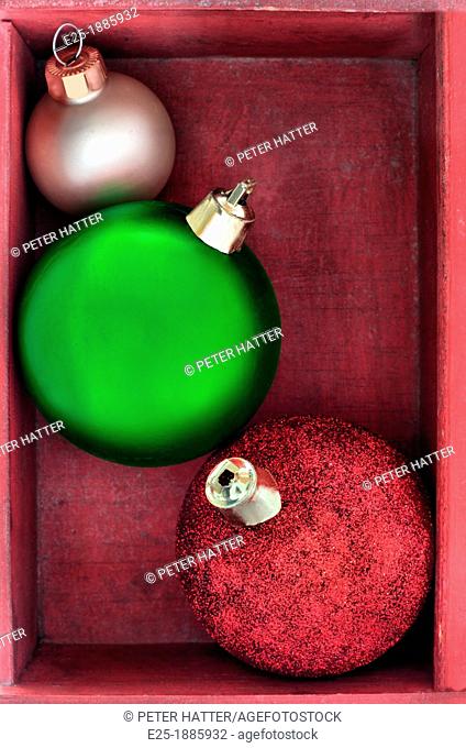Three green, red and gold Christmas baubles close up in a red wooden box