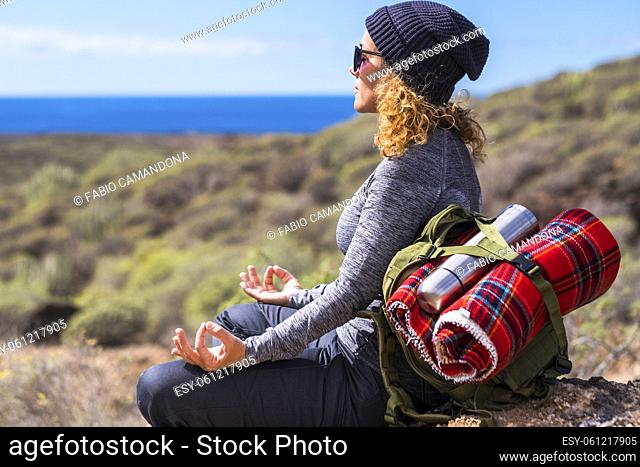 Relaxed woman in meditation position sitting on the rocks during travel backpack adventure leisure activity outdoor. Adult female enjoy active lifestyle and...