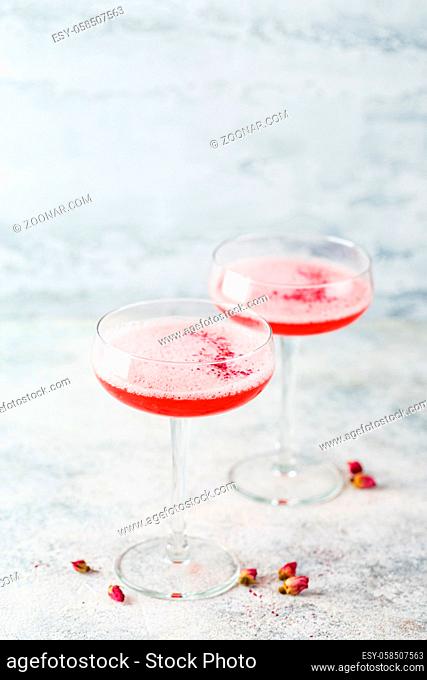 Pink alcoholic cocktail with lemonade, champagne or Martini in a champagne glass, with froth and decorated with dry rosebuds, cocktail like Daiquiri