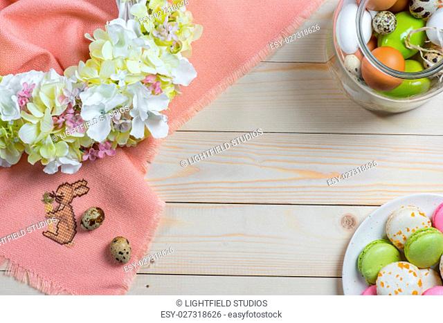 Colorful Easter eggs, tasty macarons, floral wreath and pink fabric on table