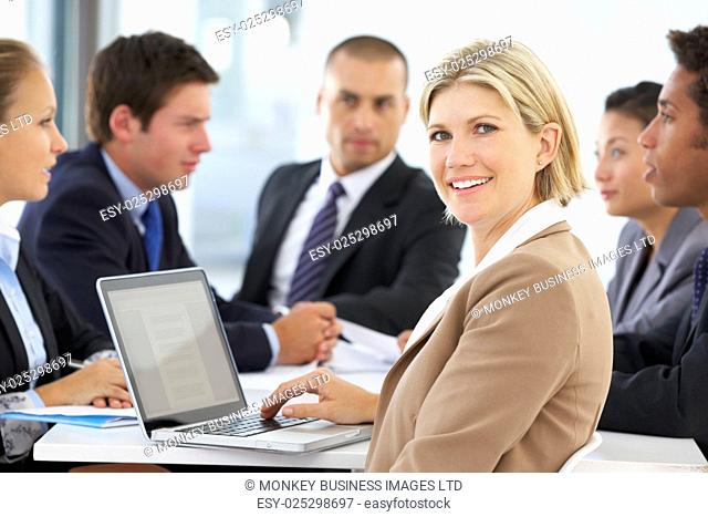 Portrait Of Female Executive With Office Meeting In Background