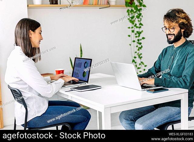 Smiling freelancers using laptops at desk in office