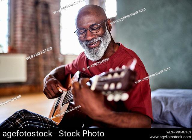 Smiling mature man playing guitar at home