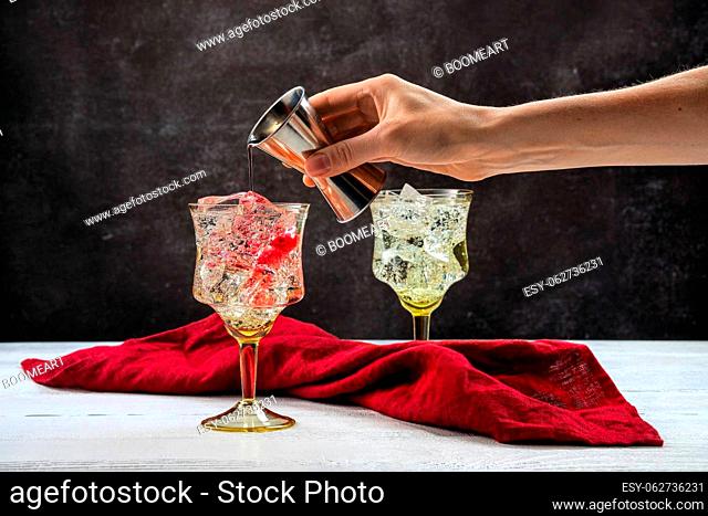 Hand of bartender with jigger pouring pomegranate bitter in cocktail with gin