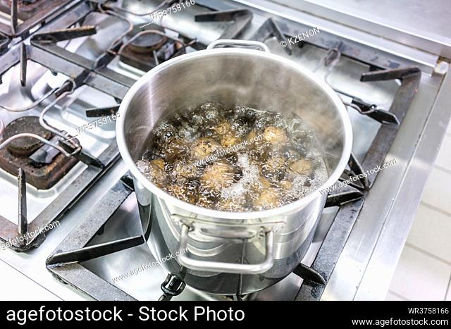 Pot with potatoes cooking on gas stove in restaurant or hotel kitchen