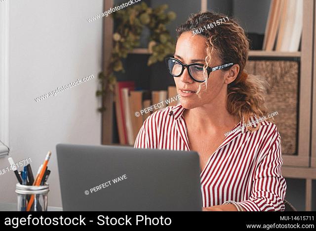 Adult female executive looking at laptop screen reading email or social media content at home office. Focused businesswoman using computer at modern office