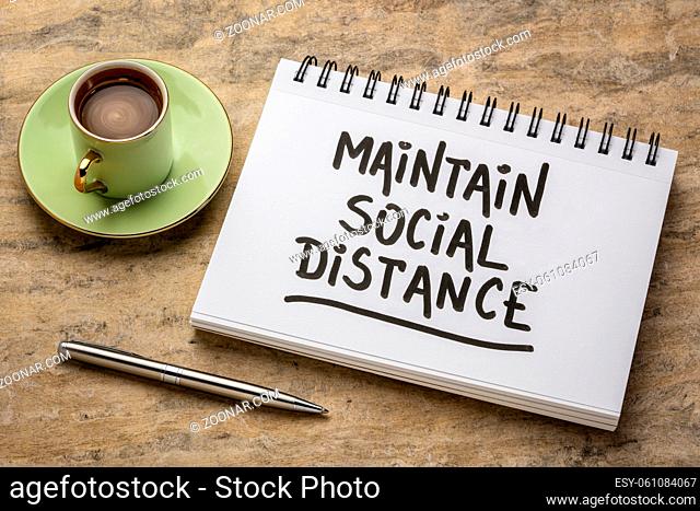 maintain social distance advice or reminder - handwriting in a spiral art sketchbook with a cup of coffee against handmade paper