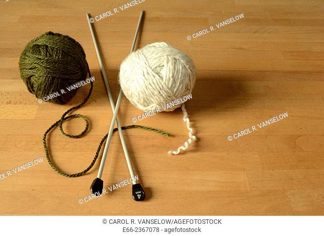 Two balls of wool (one dark green, one white) laying on table with knitting needles