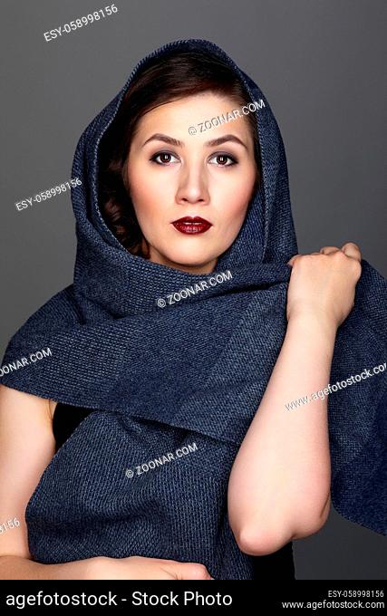 Beauty portrait of brunette woman dressed in dark blue scarf. Female portrait from a three-quarter angle on black background. Hand wraps the scarf