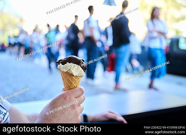 22 April 2023, Berlin: A man holds his ice cream with the varieties Whiskey Chocolate and Salted Peanut while the crowd behind him exceeds fifty
