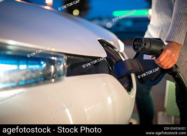 Young woman charging an electric vehicle. Car sharing concept
