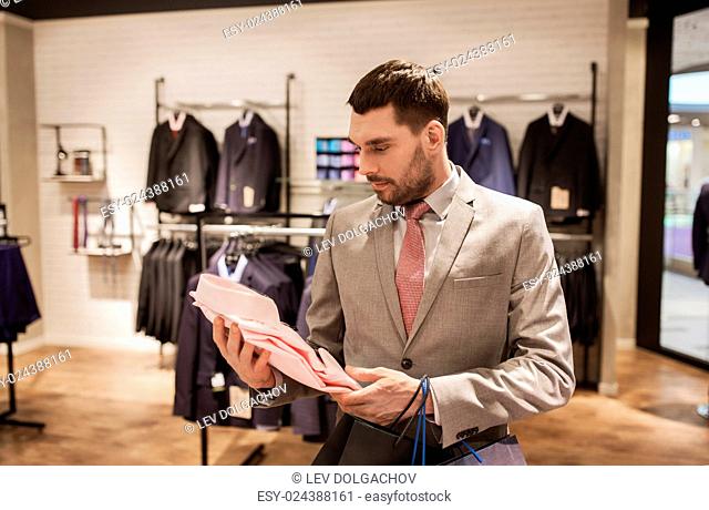 sale, fashion, style and people concept - elegant young man or businessman in suit with shopping bags choosing shirt in mall or clothing store