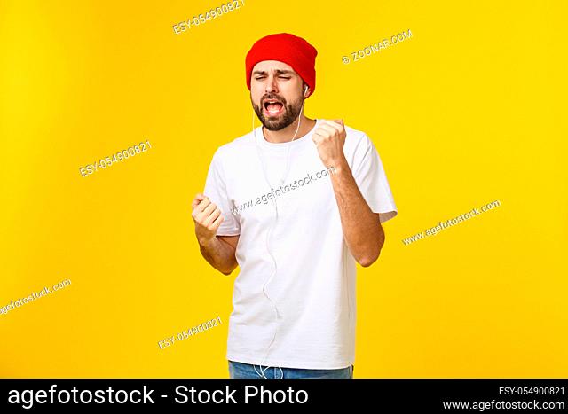 Portrait of a handsome young man dancing and listening music, isolated on yellow background