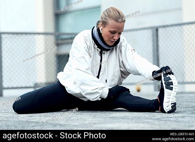 Young female athlete doing stretching exercise while sitting on ground in park