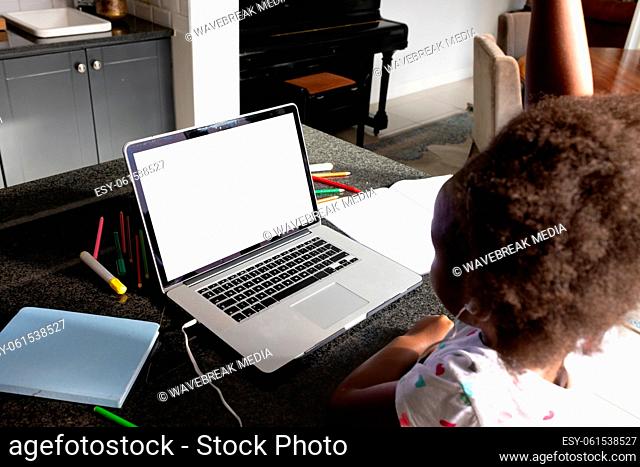 African american schoolgirl with afro hair attending online lecture over laptop on table at home
