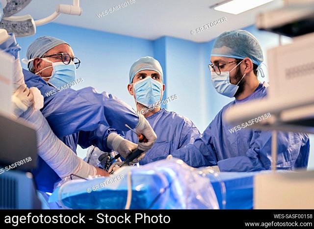 Male doctors operating surgery with surgical equipment while standing in operating room during COVID-19