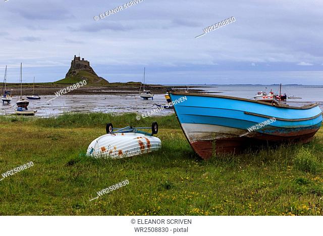 Fishing boats onshore and beach at low tide with Lindisfarne Castle and Farne Islands, Holy Island, Northumberland, England, United Kingdom, Europe