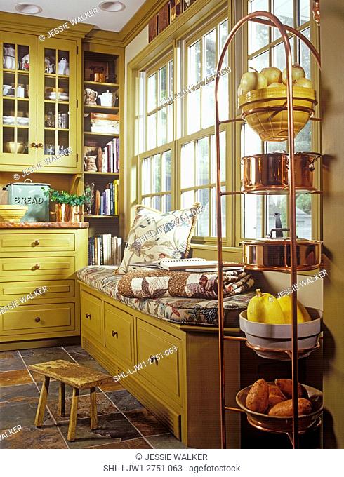KITCHENS - Window seat area in remodeled kitchen, mustard colored cabinets, copper pot rack in foreground, built in book shelf for cookbooks