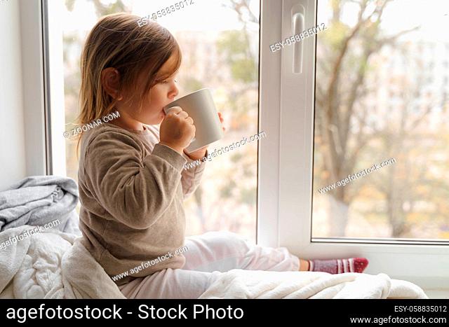 Child drink cocoa or milk near the window from big white mug. mock up of cup. christmas time. High quality photo