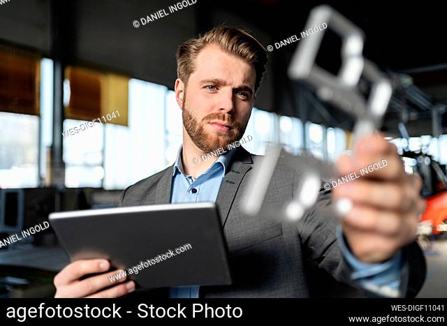 Young businessman with tablet and workpiece in a factory
