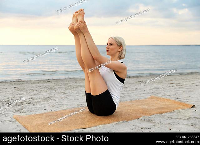 woman doing yoga boat pose on beach
