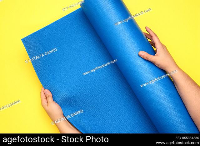 two female hands unfold a blue yoga mat, top view, yellow background