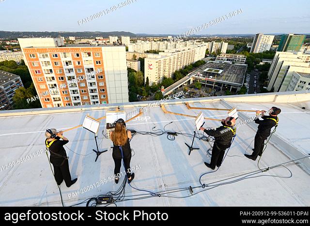 12 September 2020, Saxony, Dresden: An alphorn quartet of the Dresden Symphony Orchestra stands secured with belts on the roof of a high-rise building in the...