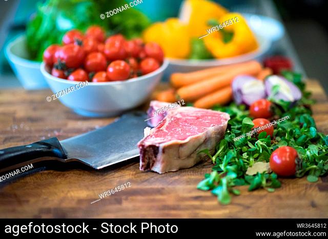 Juicy slice of raw steak with vegetables around on a wooden table