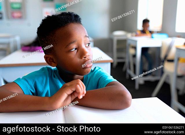 Close-up of thoughtful african american elementary schoolboy sitting at desk in classroom