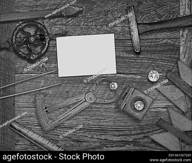 black and white image of a vintage jeweler tools and diamonds over wooden bench, space for text on a blank businesscard