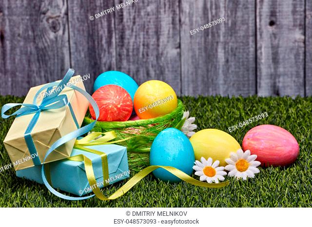 Colored easter eggs, gift boxes and flowers lying on a green grass on a grey wooden background with copy space. Greeting card, Easter background