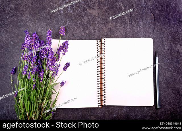 Top view of open blank notepad with lavender bouquet on black stone background, copy space for your text
