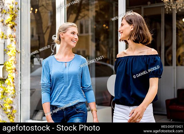 Smiling businesswomen looking at each other while walking outside office