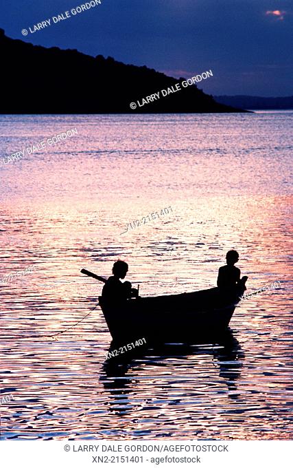 Young boys fishing from a canoe at sunset on a lake in Chile