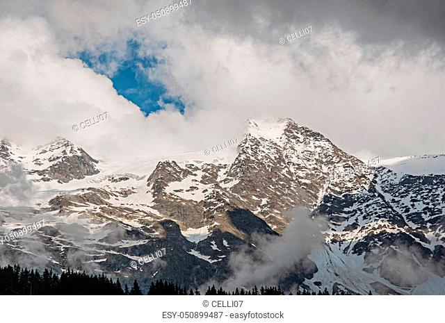 View of snowy peaks in alpine mountains landscape with blue sky and clouds at Les-Contamines-Montjoie. A small alpine village located in the Haute-Savoie...