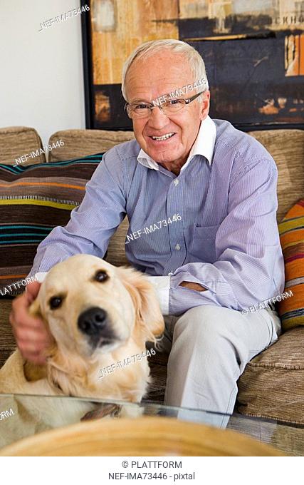 Senior man in a sofa patting a dog, Sweden