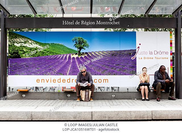 People wait at a tram stop in Lyon with an advertisement for a holiday in Provence in the background