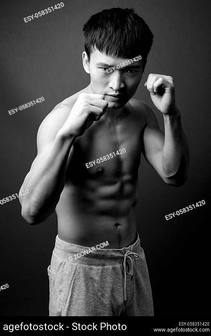 Studio shot of young Chinese man shirtless against gray background in black and white