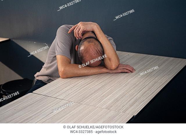 Singapore, Republic of Singapore, Asia - A man is sleeping while sitting at a table in a food court